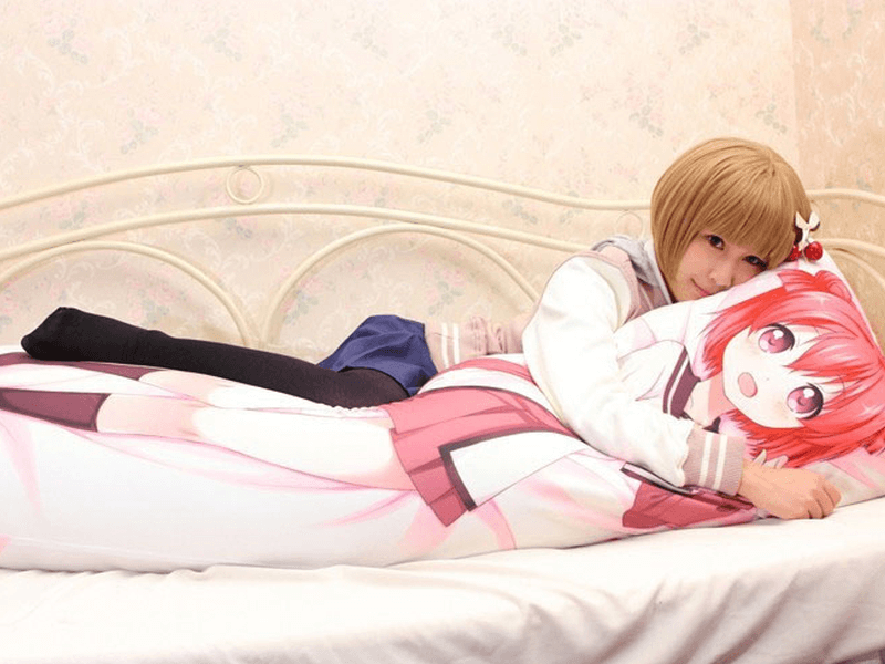 girl in schoolgirl uniform on bed hugging anime dakimakura pillow