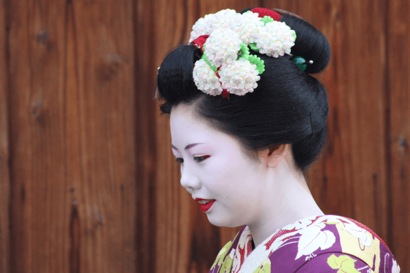 profile portrait of geisha apprentice with traditional shimada hairstyle and flowers in her hair