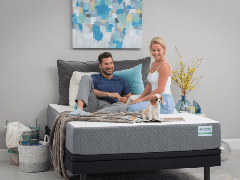 man, woman and dog sitting on GhostBed mattress with pillows and blanket