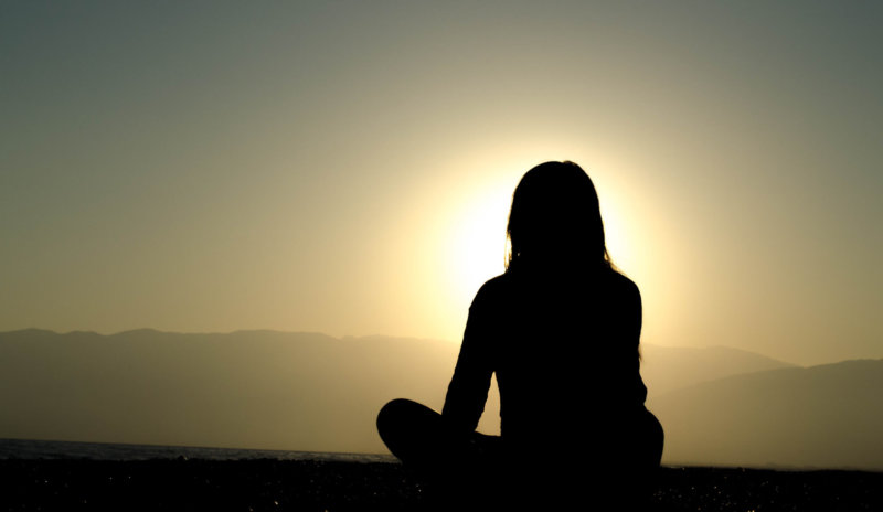 silhouette of long haired person sitting and looking at mountain view