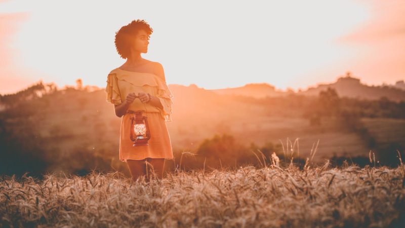 Woman carrying lamp in open field during sunset