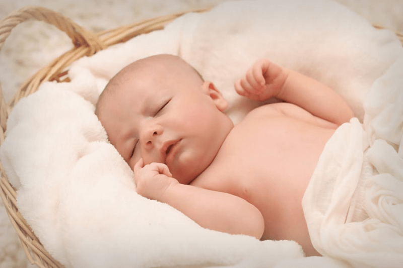 A baby sleeping soundly on a fluffy blanket, inside a wicker basket