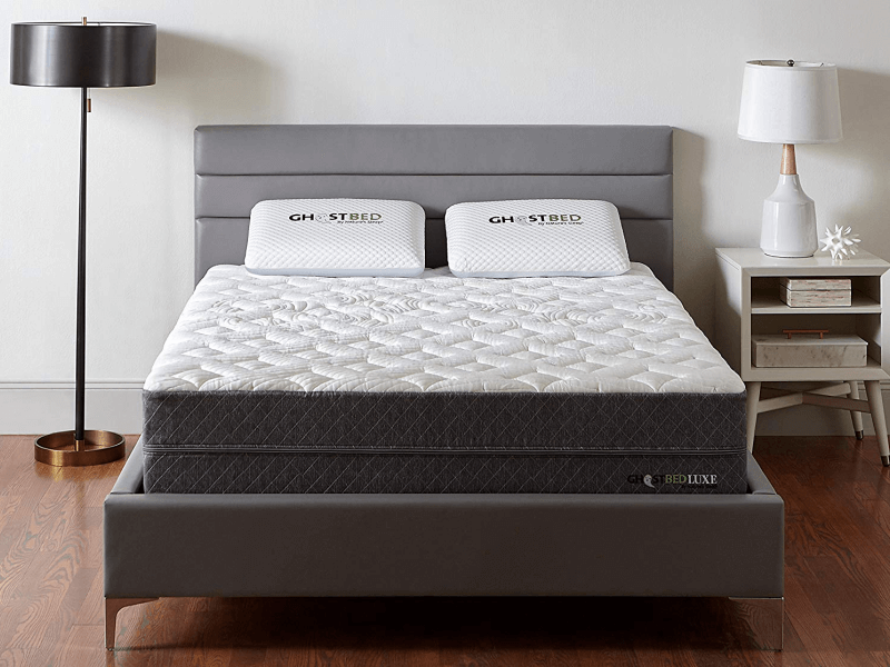 front view of GhostBed Luxe mattress on bedframe between floor lamp and bedside table with lamp